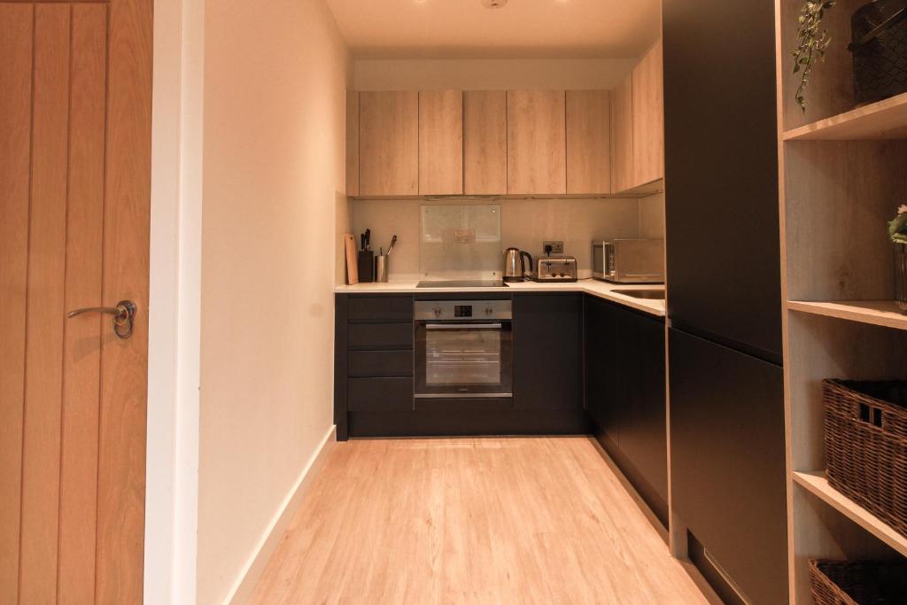 una pequeña cocina con armarios negros y suelo de madera. en Furness House by Pay As U Stay en Redhill