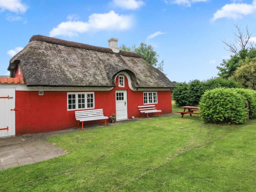 a red house with a thatched roof and two benches at Holiday Home Saarah - 25km from the sea in Western Jutland by Interhome in Bredebro
