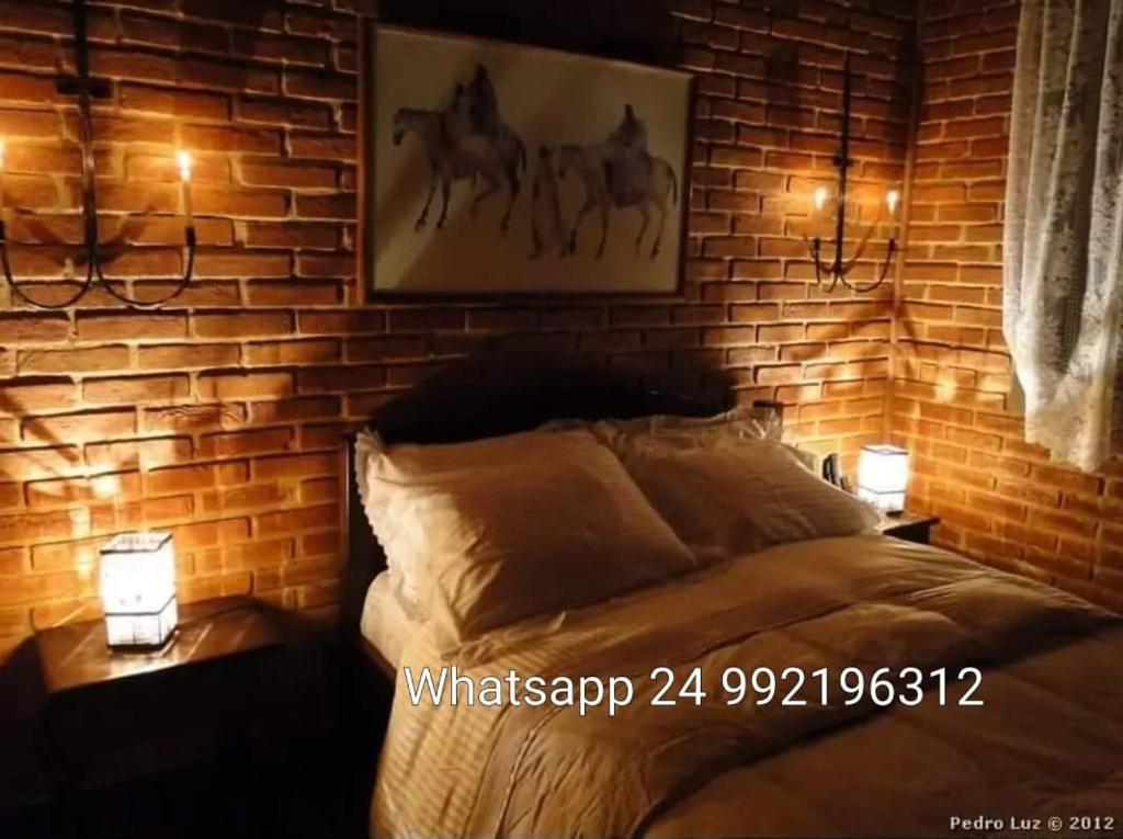 1 dormitorio con pared de ladrillo y 1 cama con 2 luces en Pousada Romântica Serra da Mata, en Penedo