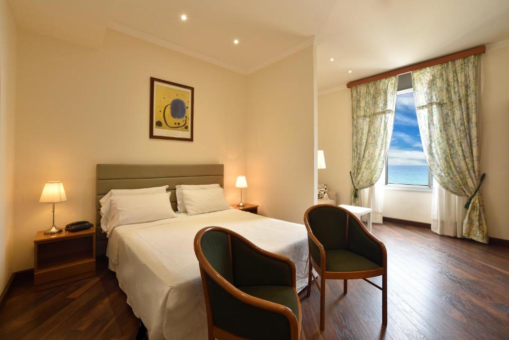 アラッシオにあるHotel Europa & Concordiaのベッド1台と椅子2脚が備わるホテルルームです。
