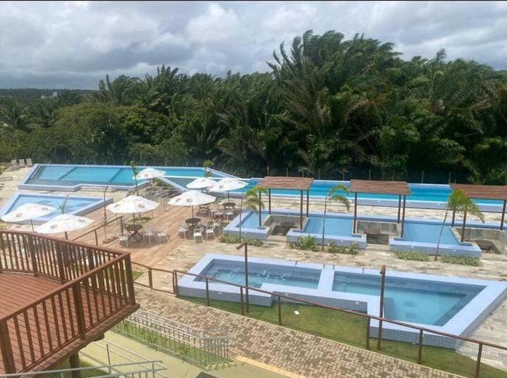 a group of swimming pools with umbrellas and tables at Apt próximo à praia de Ponta Negra/Litoral Sul/Natal in Parnamirim
