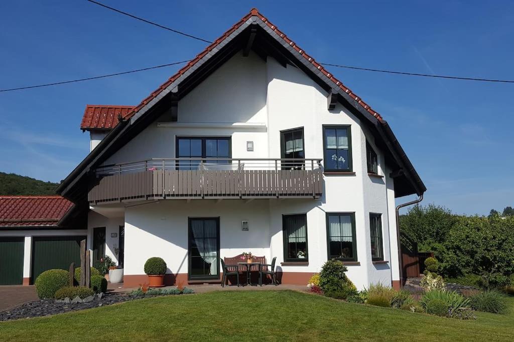 a white house with a balcony and a table at Ferienwohnung Weiherblick, Vulkaneifel in Mosbruch