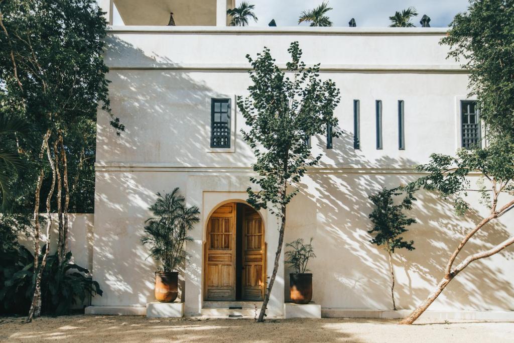 a white building with a wooden door and trees at Yum Kaax Boutique Villa in Tulum