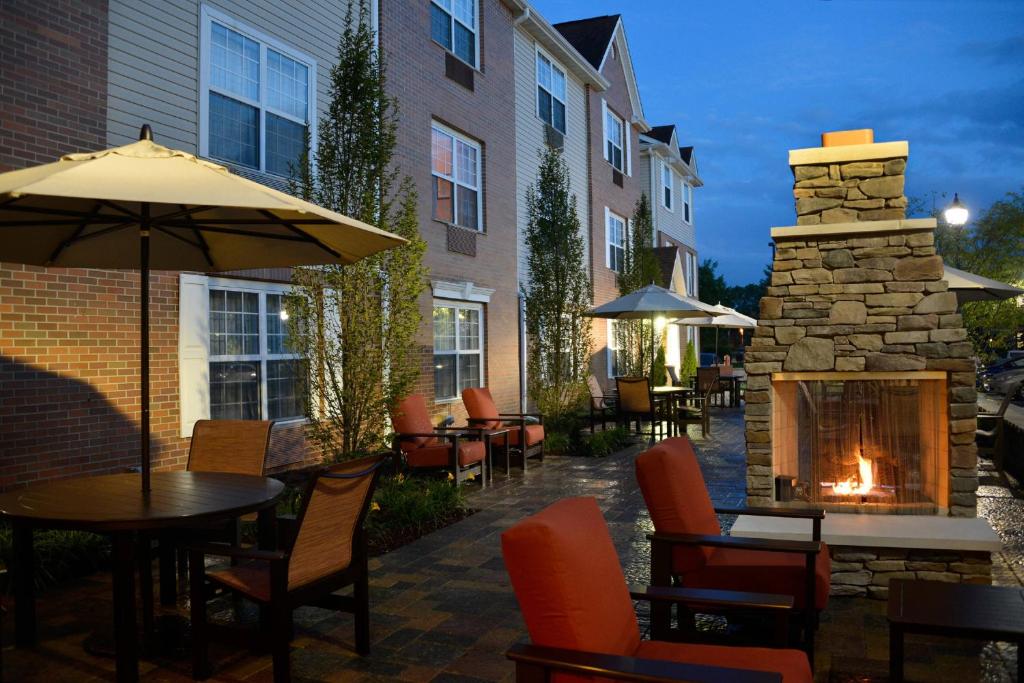 un patio con tavoli, sedie e camino in pietra di TownePlace Suites by Marriott East Lansing a East Lansing