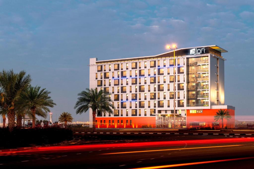 a lit up hotel with palm trees in front of it at Aloft Dubai South in Dubai