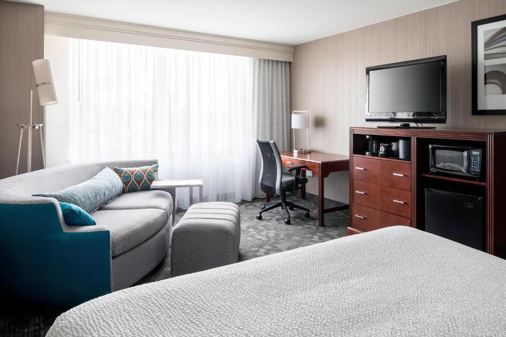 a hotel room with a couch and a desk with a television at Courtyard by Marriott Seattle Federal Way in Federal Way