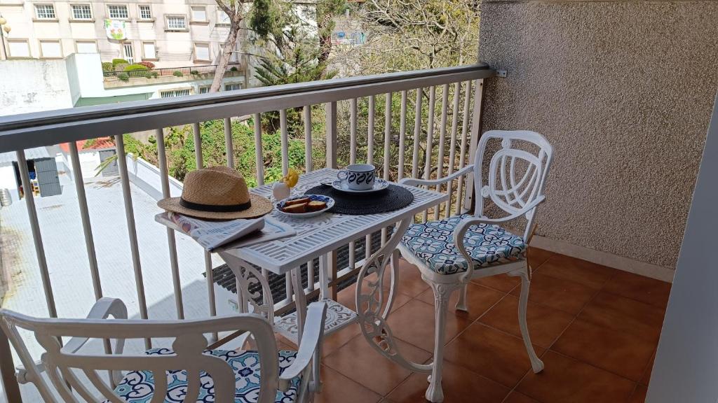 een tafel met een hoed en 2 stoelen op een balkon bij El rinconcito de la playa, parking incluido in Sanxenxo