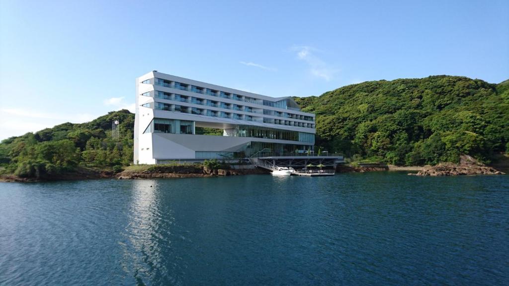 a building on a lake with a boat in the water at OliveBay Hotel in Saikai