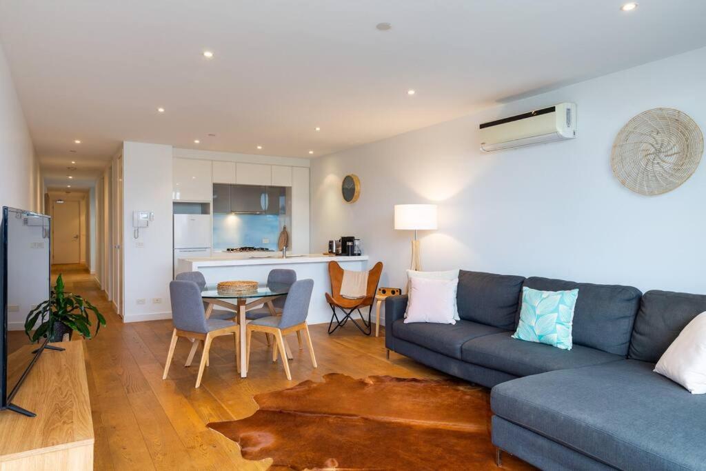 Una sala de estar con un sofá azul y una cocina. en PORT MELBOURNE - A stay at the Bay, en Melbourne