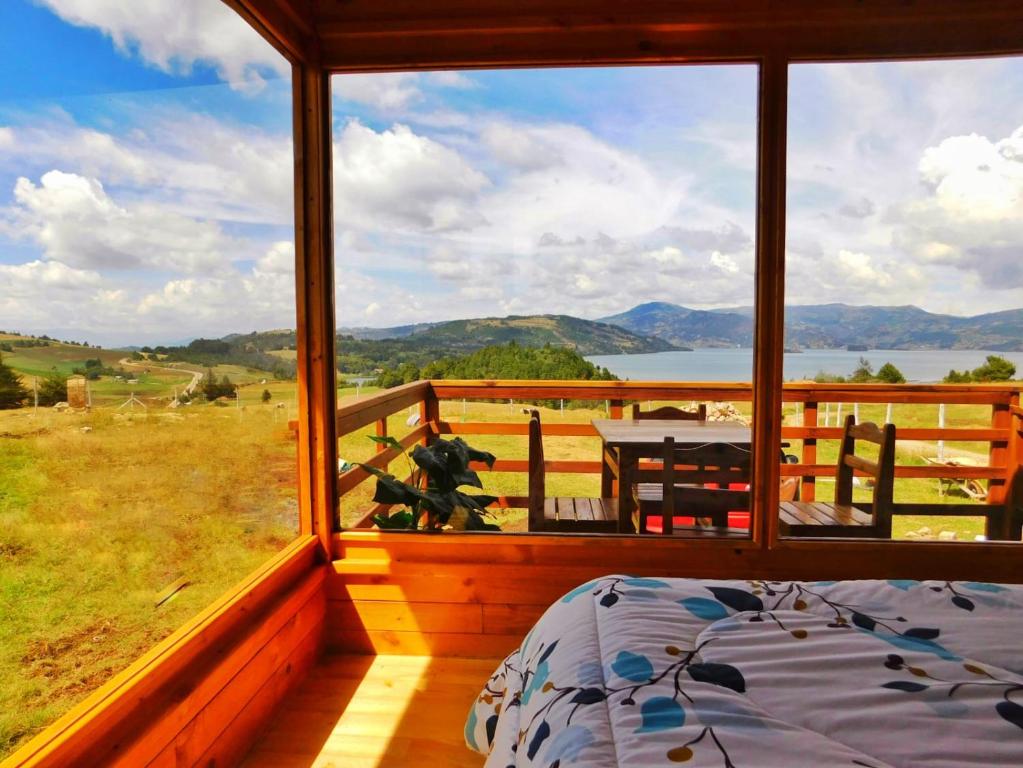 ein Schlafzimmer mit einem großen Fenster mit einem Bett und einem Tisch in der Unterkunft Cabaña con vista a la laguna de Tota in Tota