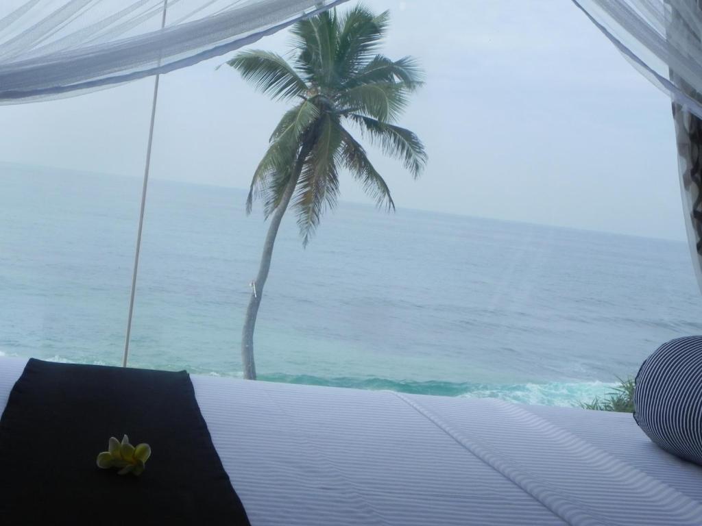 a bedroom with a view of the ocean and a palm tree at Amanda Beach Villas in Unawatuna