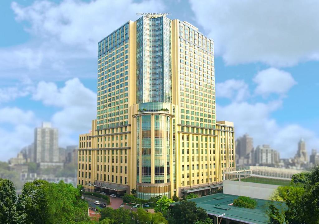 馬尼拉的住宿－New Coast Hotel Manila (formerly New World Manila Bay Hotel)，一座高大的黄色建筑,以城市为背景