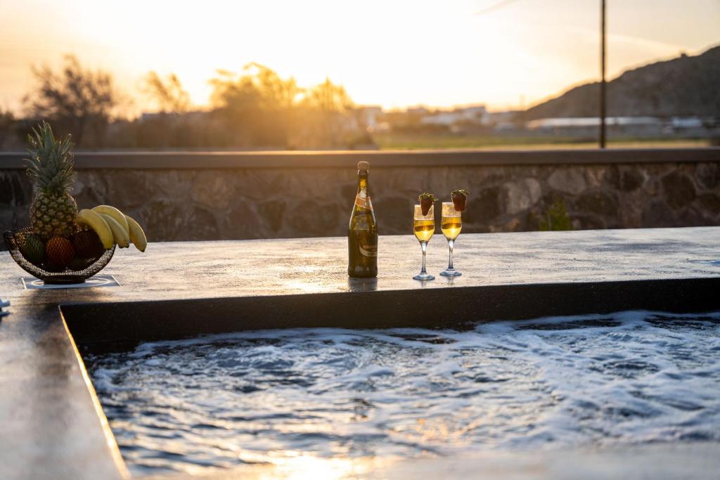 due bottiglie e bicchieri di vino seduti su un tavolo accanto alla piscina di Almira Luxury Suites a Perivolos