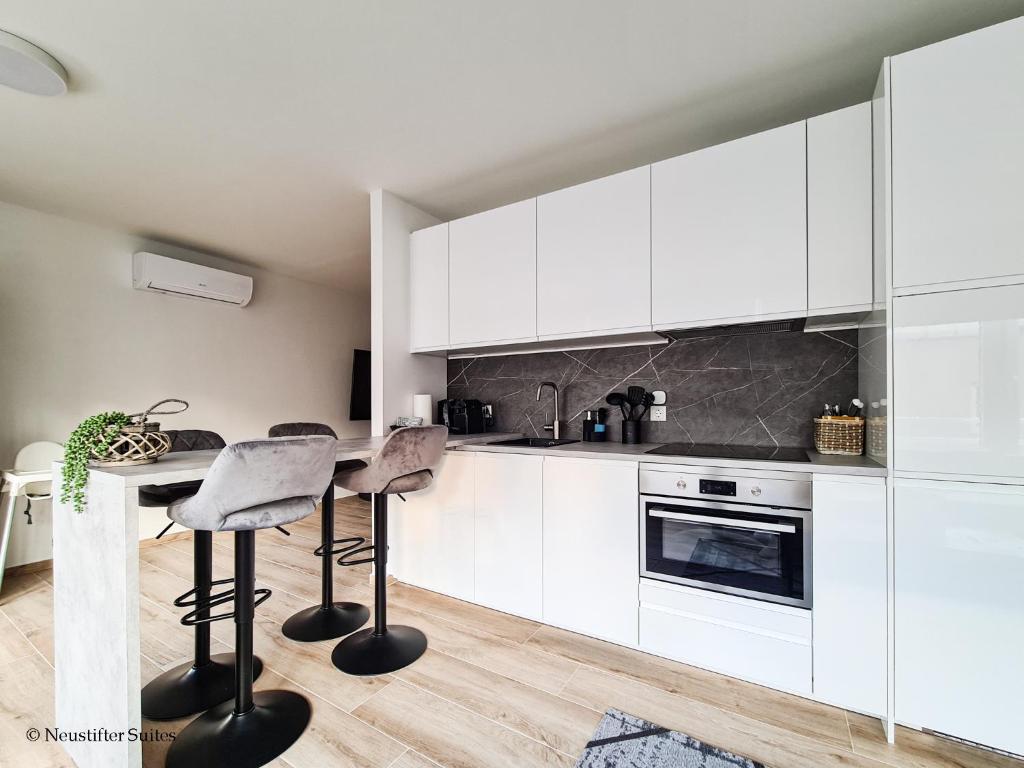 a kitchen with white cabinets and a table with stools at St. Antoni Suite 2 in Eisenstadt