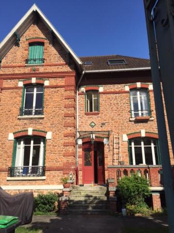 una casa in mattoni con porta rossa e finestre di Chambres cosy dans une maison meulière de charme a Saint-Maur-des-Fossés
