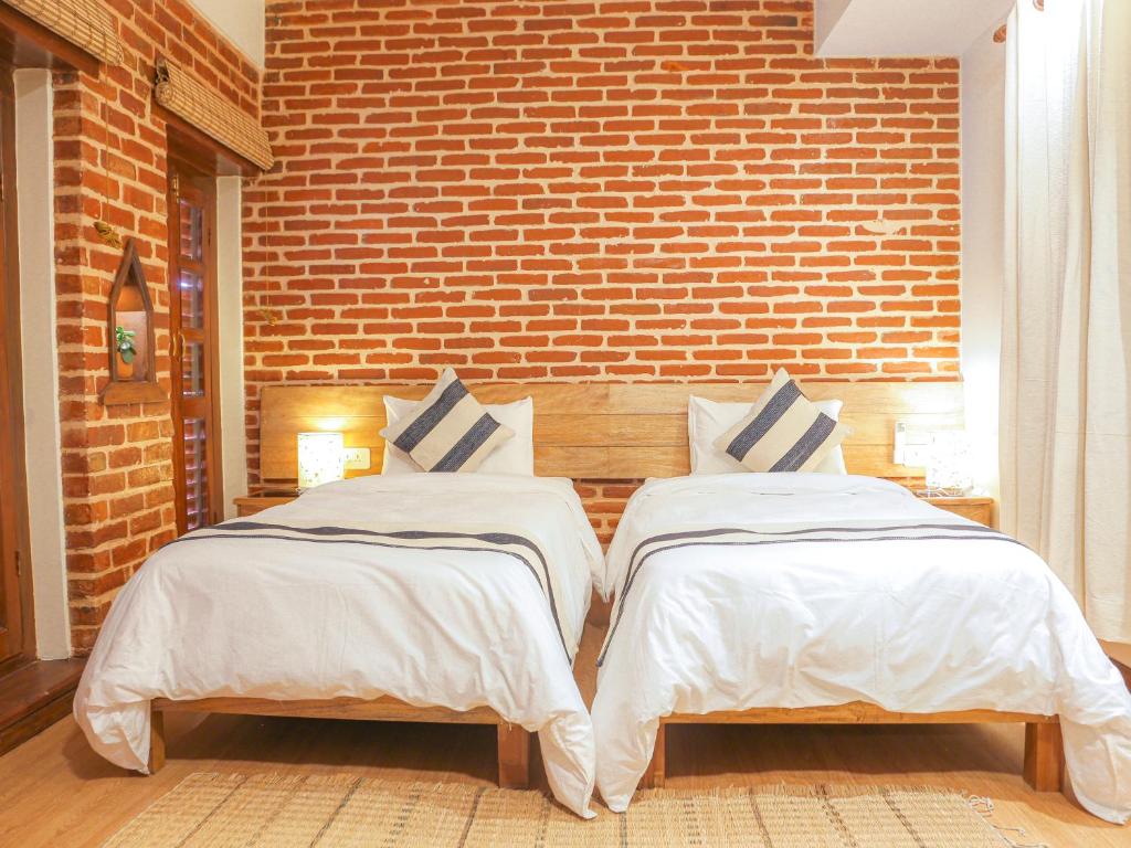 2 Betten in einem Zimmer mit Ziegelwand in der Unterkunft KGH Patan in Pātan