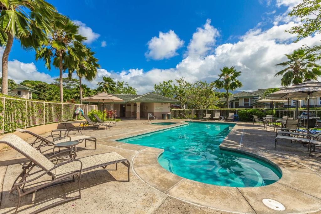 a pool with chairs and tables and palm trees at Nohea Villa in Princeville