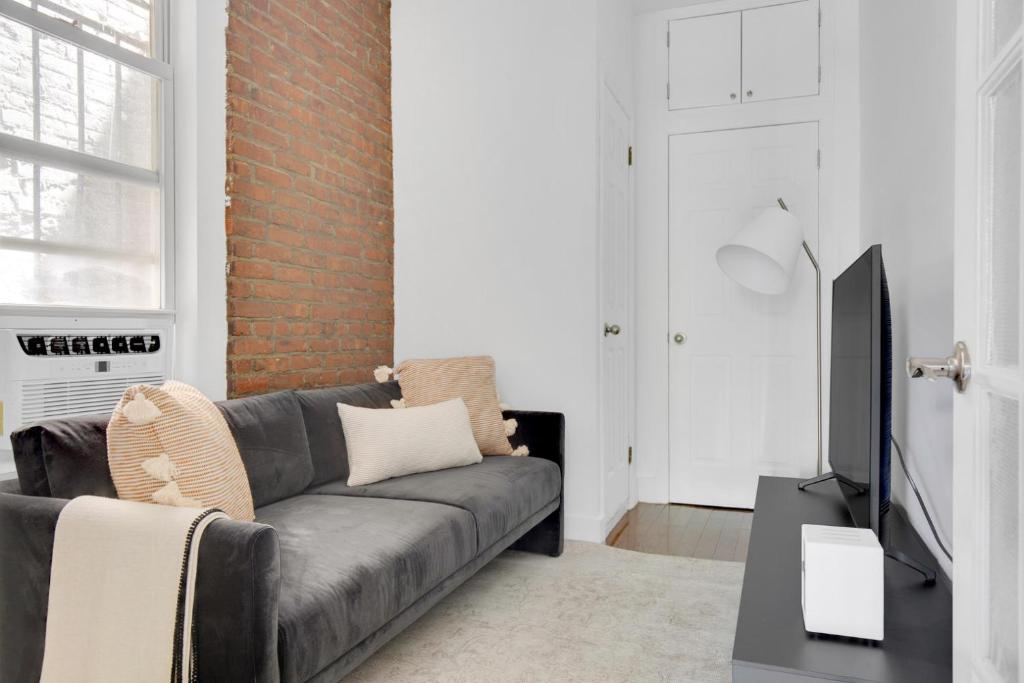 a living room with a gray couch and a brick wall at Sunlit LES 1BR w WD nr BD train NYC-865 in New York