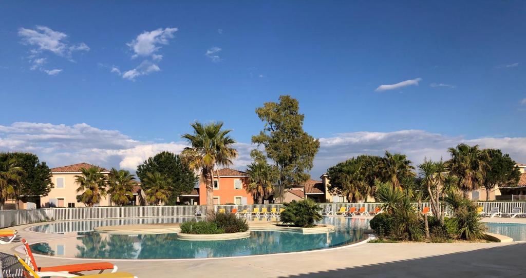 uma piscina num resort com palmeiras em Maison Le Hamac du Golf em Fabrègues