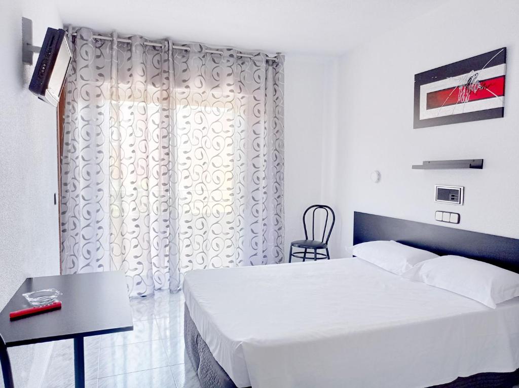 a white bedroom with a bed and a chair at Hostal Lady Ana María in Collado-Villalba
