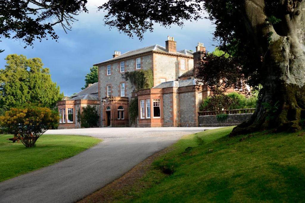 a large brick house with a tree in front of it at Mabie House Hotel in Dumfries