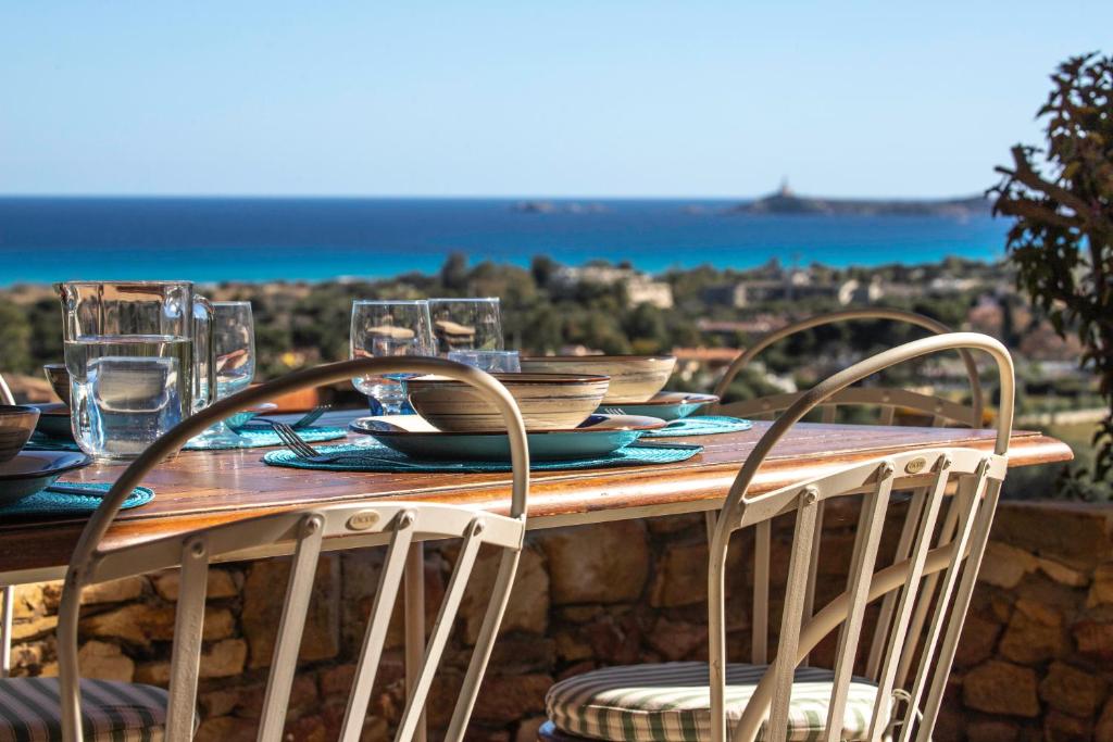 uma mesa de madeira com cadeiras, pratos e copos em Villa Corallo - FREE WIFI - 1km from the beach em Villasimius