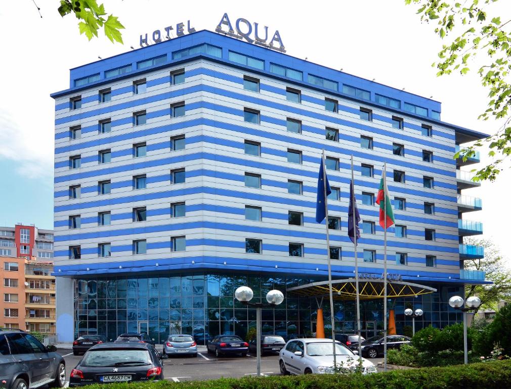 a blue hotel building with cars parked in a parking lot at Aqua Hotel in Burgas