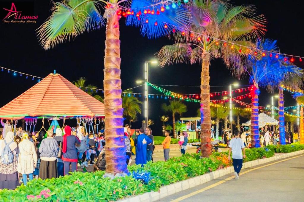 um grupo de pessoas andando em torno de um festival com palmeiras em Porto Said Tourist Resort em `Ezbet Shalabi el-Rûdi