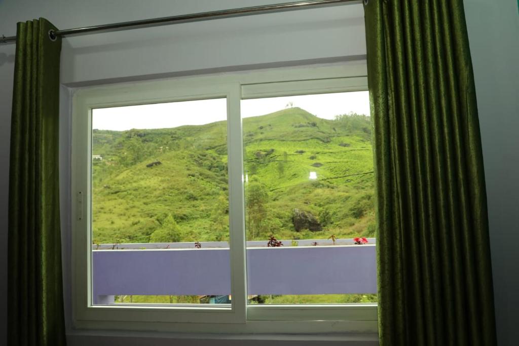 a window with a view of a green hill at Ammukutty's Cottage in Munnar