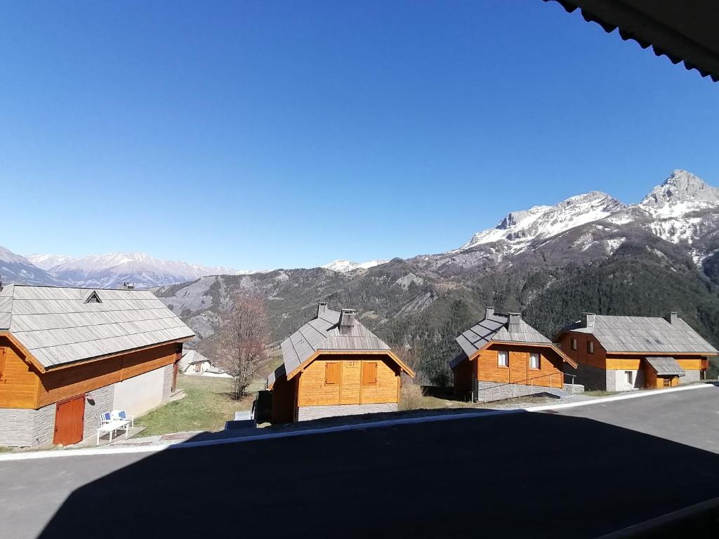 un grupo de edificios de madera con montañas en el fondo en Hameau Pra Roustan by Godille, en Pra-Loup