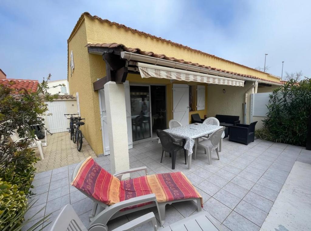 un patio con mesa y sillas frente a una casa en Charmante Villa de vacances, en Cap d'Agde