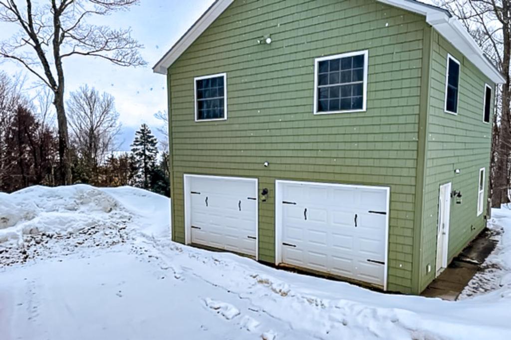 une maison verte avec deux portes de garage dans la neige dans l'établissement Lake Adventures, à Greenville