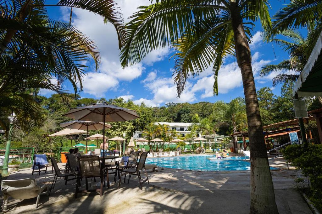 a pool with palm trees and a table and chairs at Hotel Green Hill in Juiz de Fora