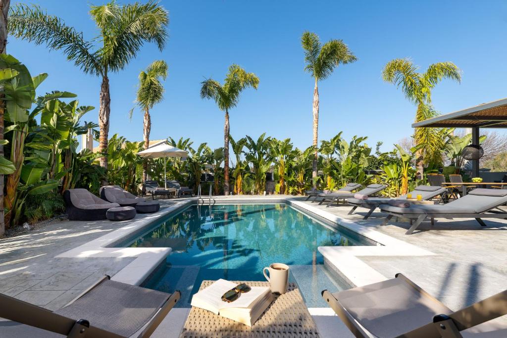 una piscina con tumbonas y palmeras en Palmeral Luxury Suites en Rodas
