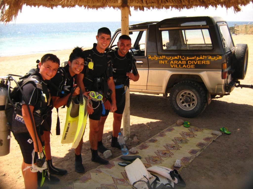 a group of people standing under an umbrella on the beach at Arab Divers Dive Center and Bed & Breakfast in Aqaba
