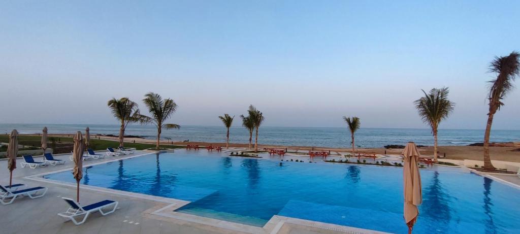 a swimming pool next to the ocean with palm trees at The Beach House in Muscat