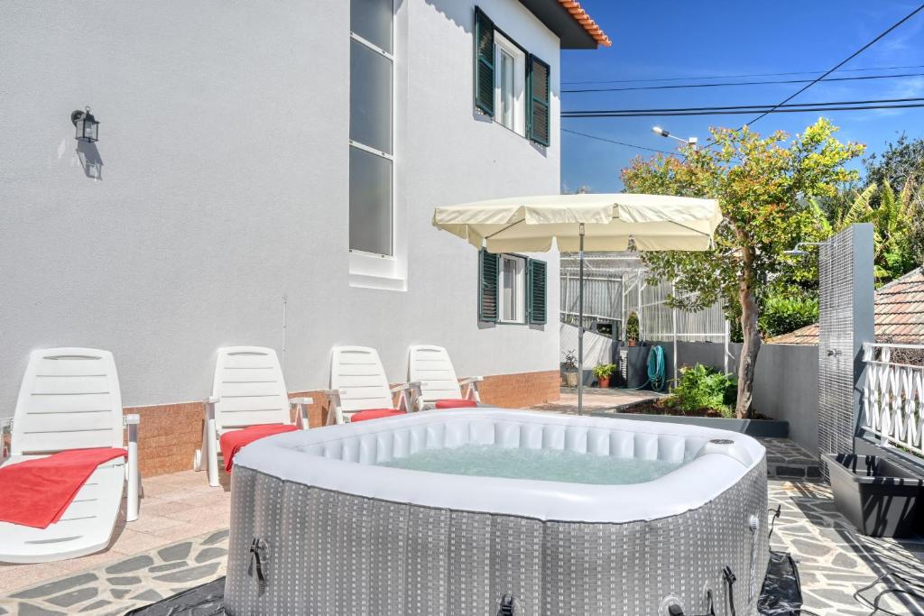 a hot tub in a backyard with chairs and an umbrella at Casa do Valentim, a Home in Madeira in Ponta do Sol