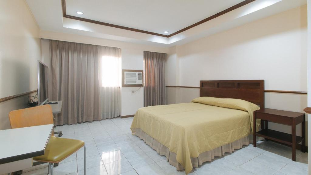 a bedroom with a bed and a table and a desk at Garden Plaza Hotel Manila in Manila