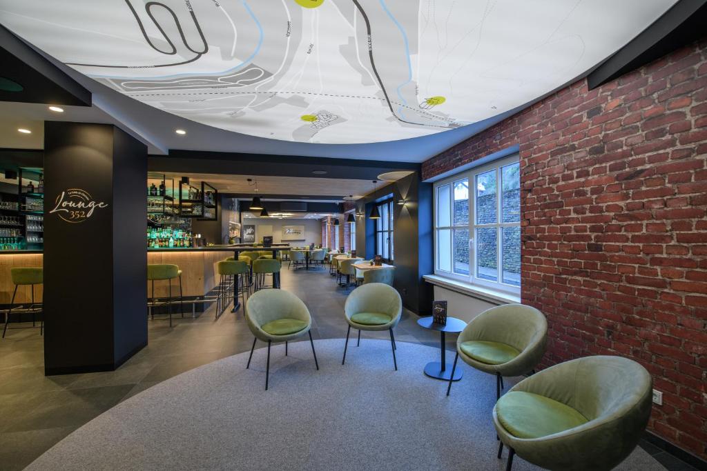 a restaurant with green chairs and a brick wall at Hotel du Commerce - Restaurant La Table de Clervaux in Clervaux