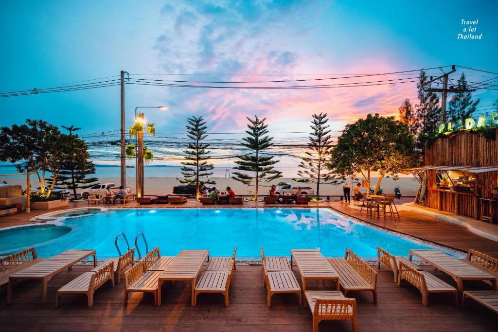 a swimming pool with tables and chairs in front of a sunset at Zand Morada Pattaya in Jomtien Beach