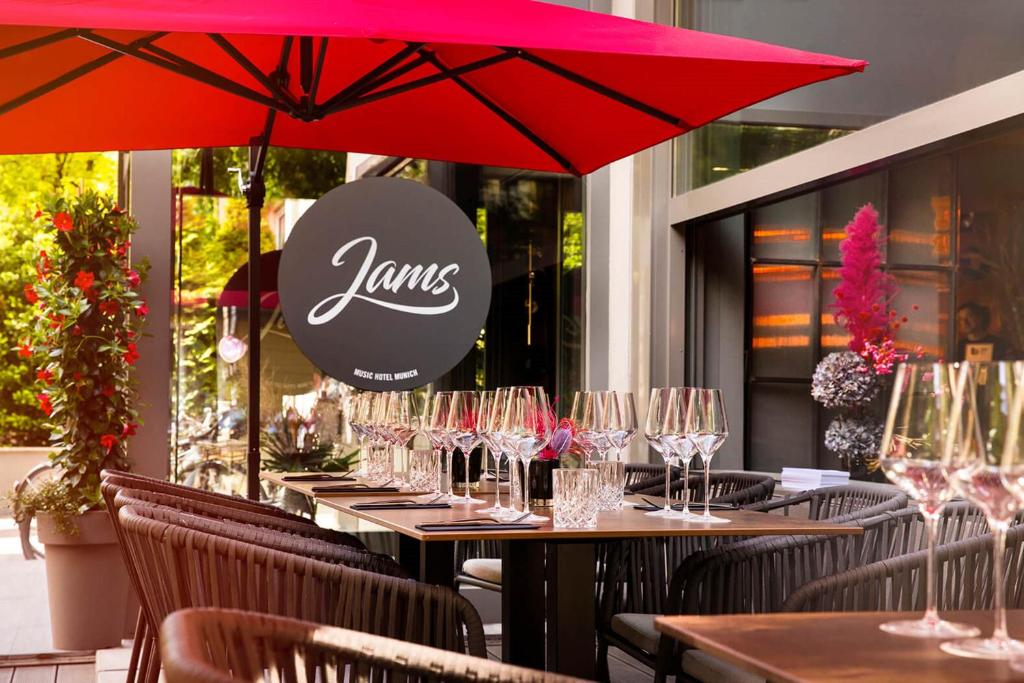 um restaurante com mesas com copos de vinho e um guarda-chuva vermelho em JAMS Music Hotel Munich em Munique