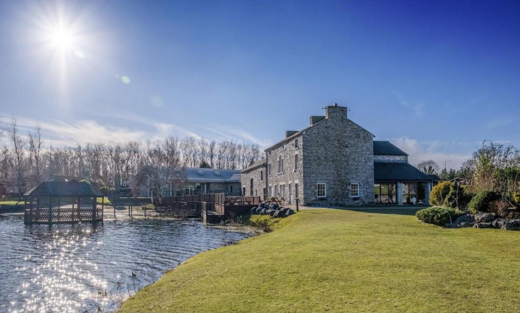 BorwickにあるBorwick Lakes Holiday Caravan (Partial Lake View)の水の横の大きな石造りの建物