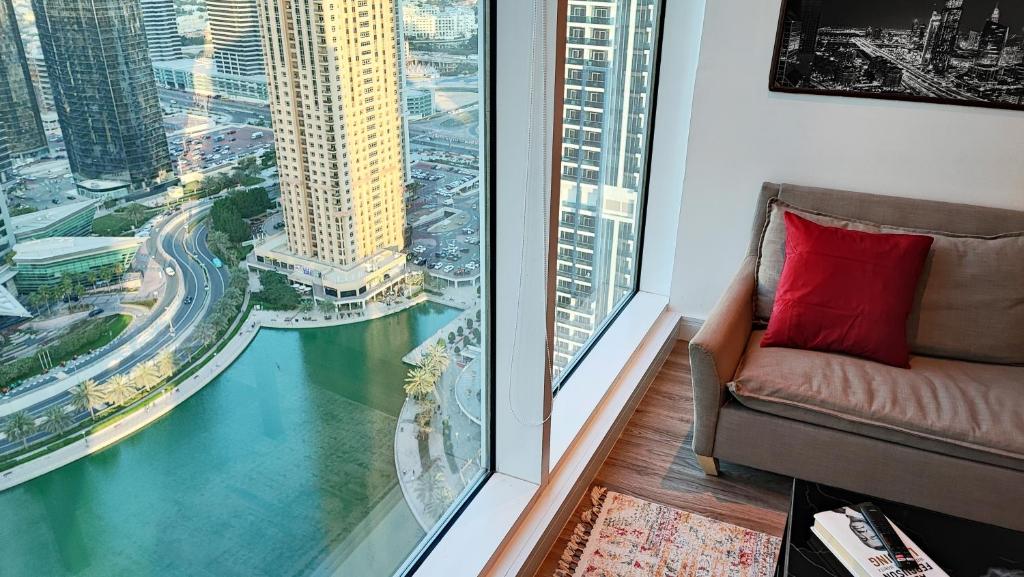 a chair with a red pillow in a room with a window at Modern & Spacious 2-Bed Condo with Panoramic Lake Views, Dual Balconies, Steps from Dubai JLT Metro By "La Buena Vida Holiday Homes" in Dubai
