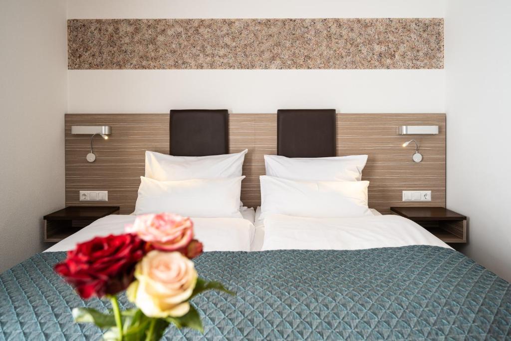 a bedroom with two beds and a vase with roses at Hotel Drei Rosen in Moosburg