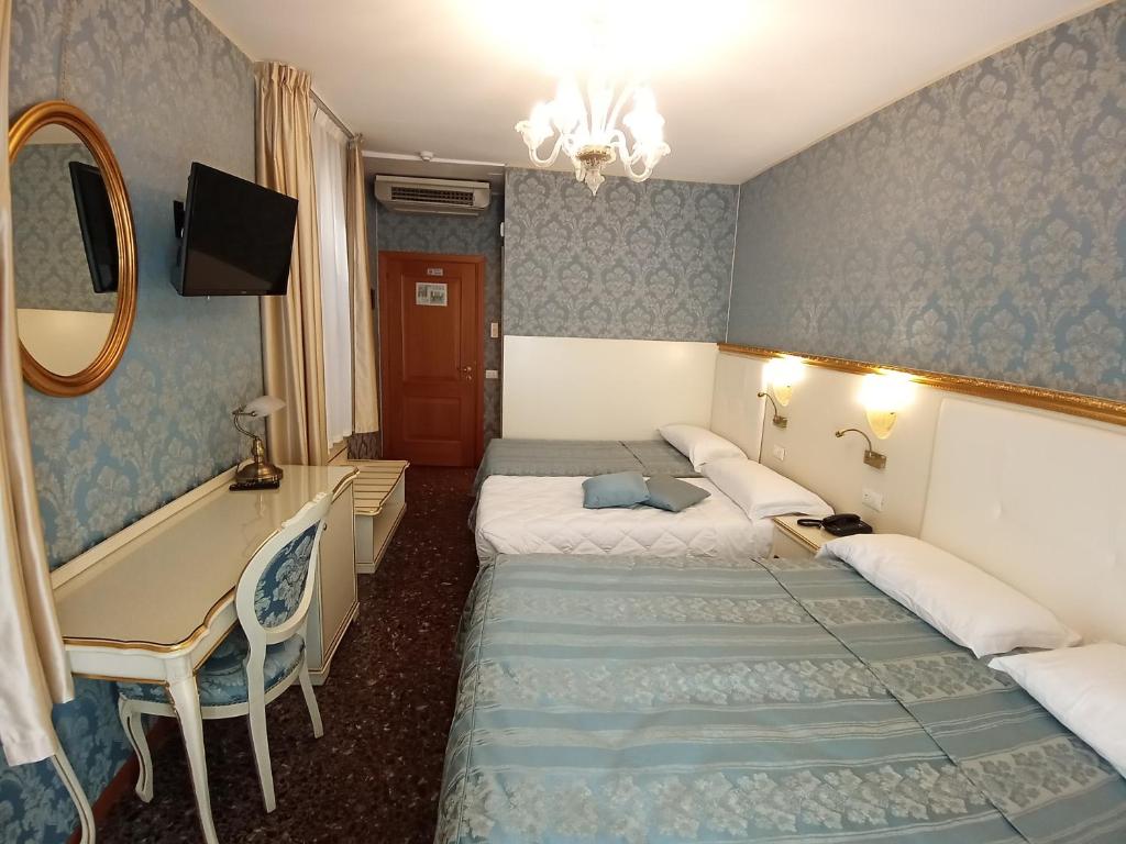 a hotel room with two beds and a desk at Hotel Il Mercante di Venezia in Venice
