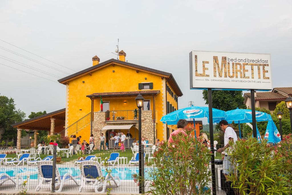ein gelbes Gebäude mit Tischen und Stühlen und einem Schild in der Unterkunft Le Murette appartamenti in Affi