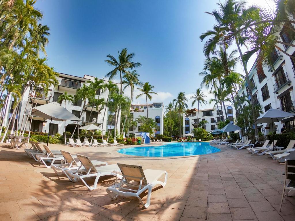 a resort with chairs and a swimming pool and palm trees at Puerto de Luna Pet Friendly and Family Suites in Puerto Vallarta