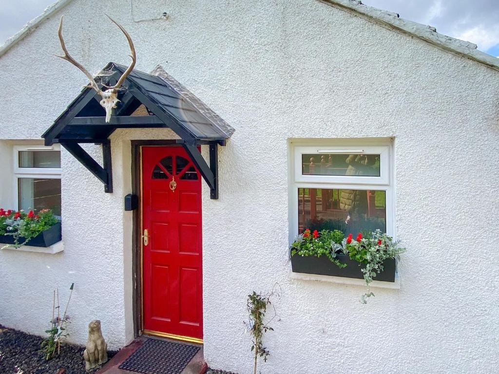 a white house with a red door and a window at Riverside Cottage in Drumnadrochit