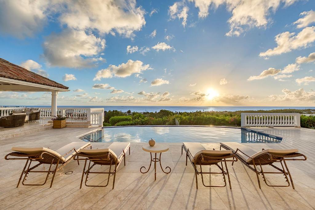 un patio avec des chaises et une piscine avec l'océan en arrière-plan. dans l'établissement Villa Mer Soleil, à Marigot
