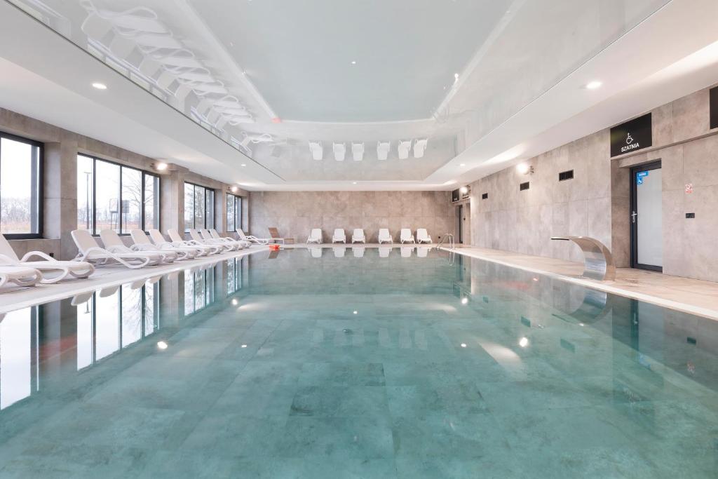 duży basen z białymi krzesłami w budynku w obiekcie Apartament AQUA BLUE Bridge Apartments & Spa z basenem Dziwnów EPapartamenty w Dziwnowie